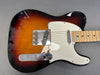 Electric guitar with sunburst finish, white pickguard, chrome hardware, and maple fretboard on gray background
