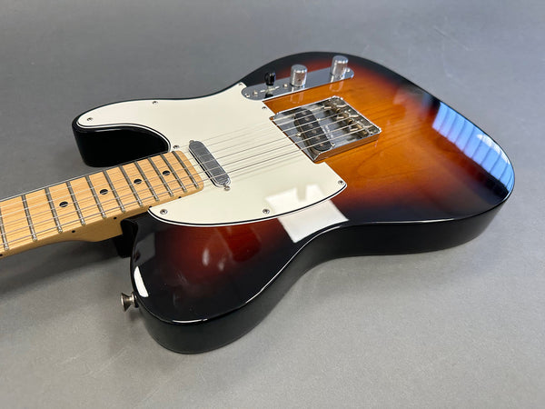 Electric guitar with sunburst finish, white pickguard, maple neck, and chrome hardware on gray background