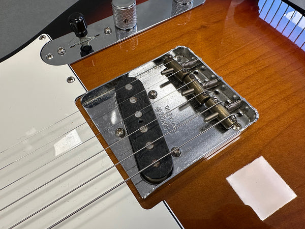 Close-up of bridge and pickup on a Fender Telecaster electric guitar with sunburst finish and white pickguard