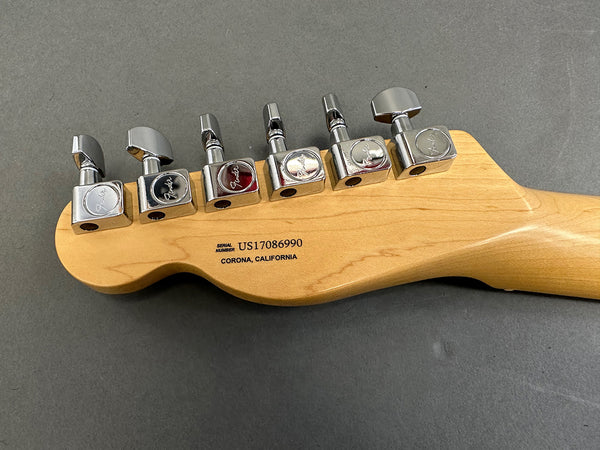 Close-up of Fender electric guitar headstock back with six chrome tuning pegs and serial number US17086990 from Corona, California on light wood finish