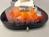 Close-up of sunburst electric guitar body with chrome bridge, white pickguard, and control knobs on gray surface