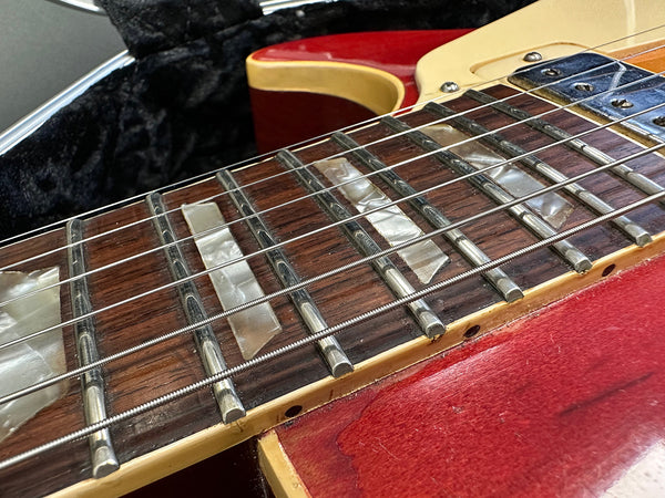 Close-up of red electric guitar neck with pearl inlay fret markers and metal strings in guitar case interior