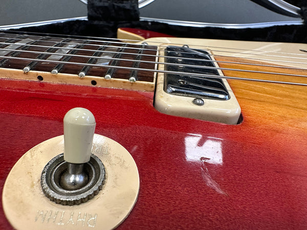 Close-up of red electric guitar body showing toggle switch, pickup, and fretboard details with wood grain finish
