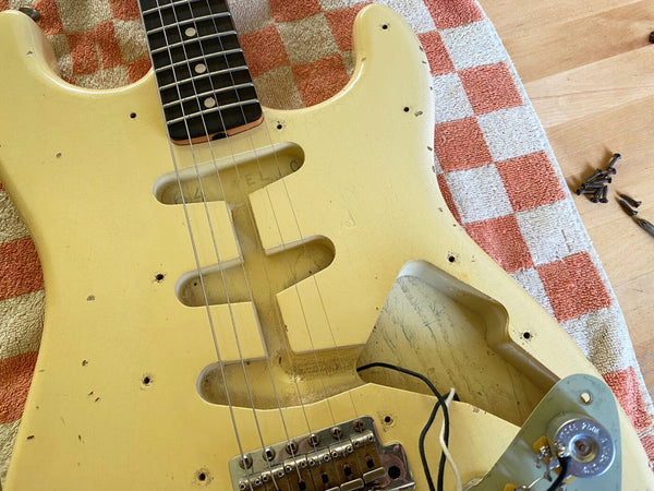 Close-up of vintage cream-colored electric guitar body with missing pickups and visible wiring on checkered red and white towel