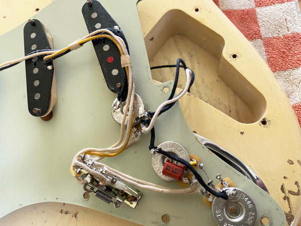 Close-up of vintage electric guitar pickguard with exposed wiring, pickups, potentiometers, and capacitor on aged cream guitar body