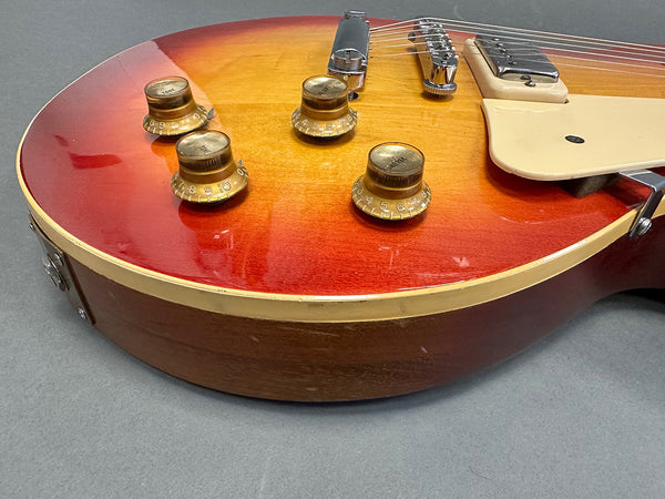 Close-up of vintage sunburst electric guitar body showing tone and volume control knobs, chrome bridge, and cream-colored pickguard on gray background