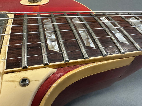 Close-up of vintage electric guitar fretboard with pearl inlays, metal frets, aged binding, and red body showing wear and patina