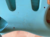 Close-up of worn light blue guitar body marked "RELIC" with a vintage-style finish and pickup cavities visible