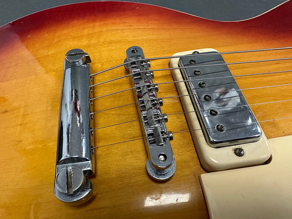 Close-up of sunburst electric guitar bridge, chrome tailpiece, adjustable saddle, and humbucker pickup with cream-colored mounting ring on a wooden body
