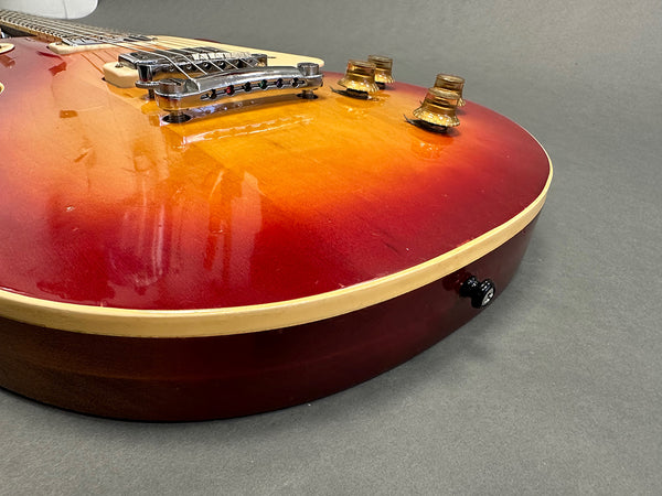 Close-up of sunburst electric guitar body showing bridge, control knobs, and strap button on gray background