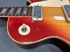 Close-up of red sunburst electric guitar body showing pickup, rhythm switch, and part of the rosewood fretboard with pearl inlays