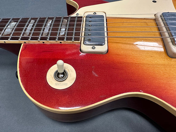 Close-up of red sunburst electric guitar body showing pickup, rhythm switch, and part of the rosewood fretboard with pearl inlays