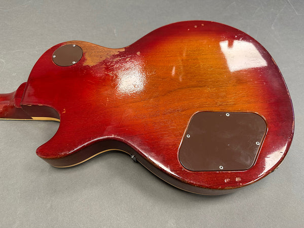 Back view of vintage red burst electric guitar body with worn finish and plastic control cavity covers on gray background