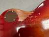 Close-up of worn red and sunburst electric guitar body showing finish wear and back control cavity cover with screws