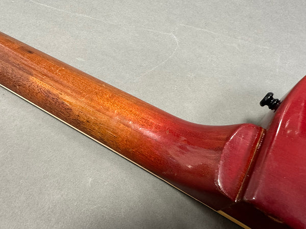 Close-up of worn red guitar neck and heel with wooden finish on gray background
