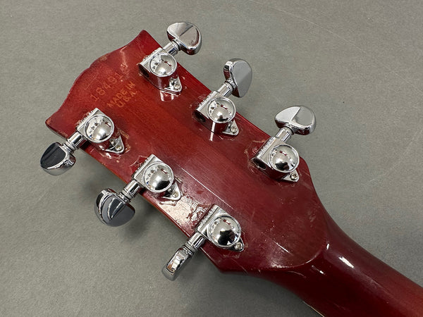 Back of red guitar headstock with six chrome tuning pegs on gray background, showing serial number and "Korea" stamp.