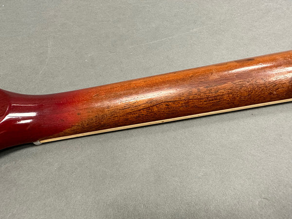 Close-up of finished wooden guitar neck with a glossy red to natural wood gradient on gray background