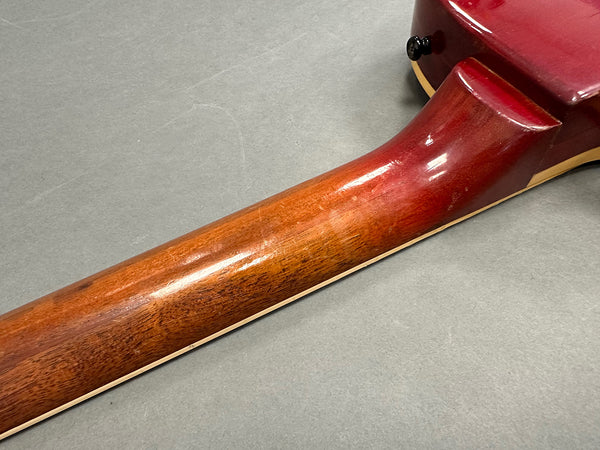 Close-up of wooden guitar neck and heel joint with red finish and cream binding against gray background