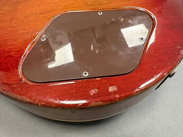 Close-up of guitar backplate cavity cover and worn edges on red electric guitar body showing wood finish wear and scratches