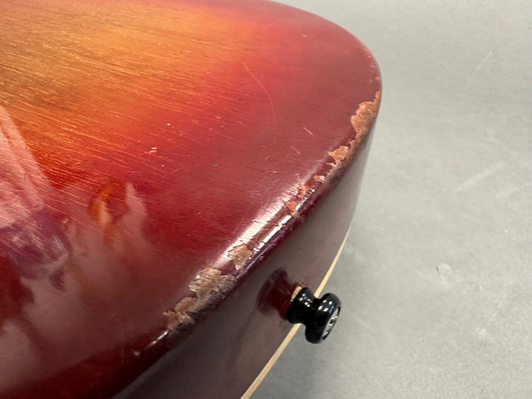 Close-up of worn and chipped edge on red sunburst electric guitar body near black strap button showing finish damage and wood exposure