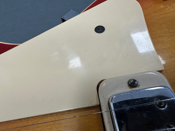 Close-up of vintage electric guitar body showing cream pickguard and metal pickup cover with single coil pickup and guitar string.