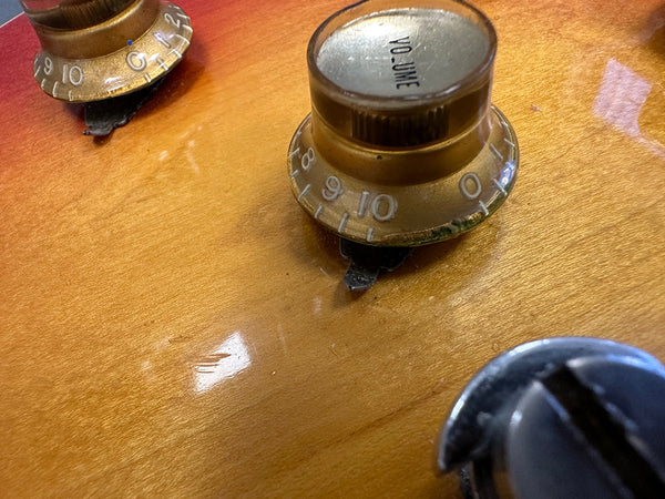 Close-up of vintage guitar volume knob and tone knob on sunburst electric guitar body with visible wear and scratches