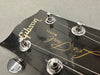 Close-up of Gibson Les Paul Model guitar headstock with tuning pegs and strings on grey background