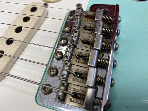 Close-up of Fender electric guitar bridge and pickup with light blue body and white pickguard showing steel strings and adjustable saddles