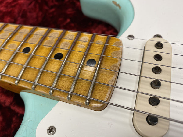 Close-up of vintage electric guitar maple fretboard with worn frets, black dot inlays, and single-coil pickup on seafoam green body with white pickguard and steel strings