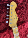 Close-up of Fender Stratocaster guitar headstock with six tuning pegs on a red plush background