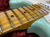 Close-up of vintage maple guitar neck and fretboard with black dot inlays on a light blue electric guitar body resting on red plush lining