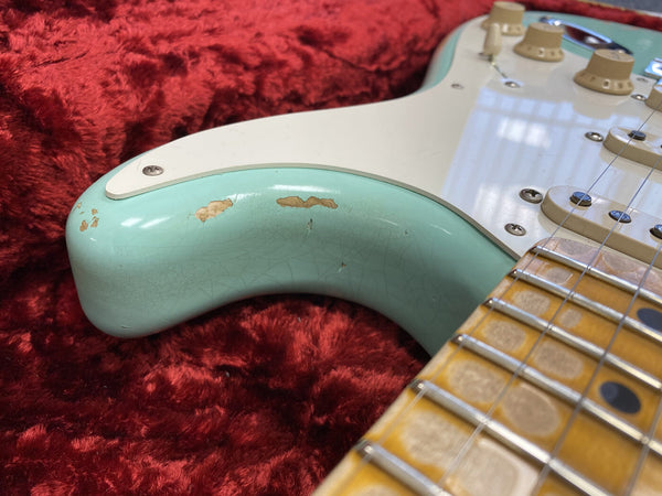 Close-up of teal vintage electric guitar body with worn paint and cracked finish next to maple fretboard on red plush fabric background
