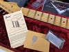 Close-up of Fender Stratocaster guitar neck with vintage maple fretboard, accompanying Fender tremolo springs instruction sheet, metal key on envelope, chrome pickup cover, and Fender Custom Shop case lining in red plush material.