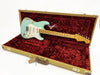 Fender Stratocaster electric guitar in seafoam green finish with worn vintage relic look, displayed inside open tweed hard case with red plush interior lining.