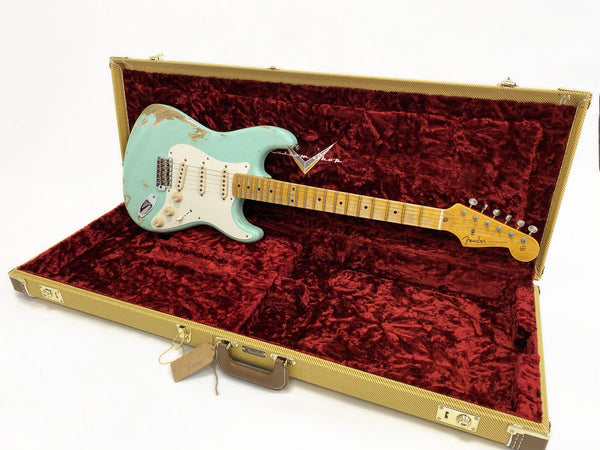 Fender Stratocaster electric guitar in seafoam green finish with worn vintage relic look, displayed inside open tweed hard case with red plush interior lining.