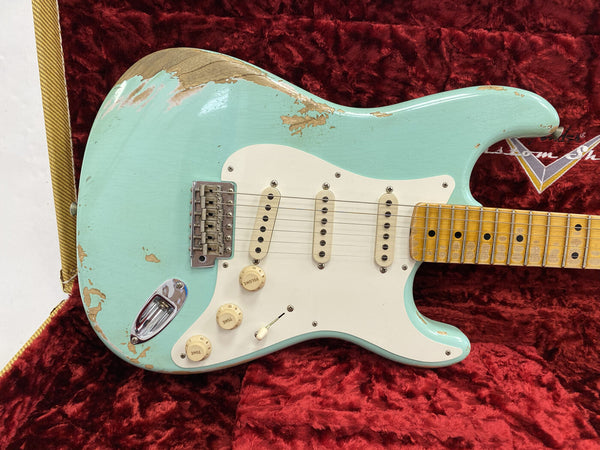 Vintage light blue Fender Stratocaster electric guitar with worn finish and maple neck, displayed on red plush guitar case interior.