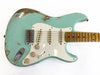 Close-up of a vintage light blue relic electric guitar with three single-coil pickups, worn wood finish, white pickguard, and maple neck with dot inlays against a white background.