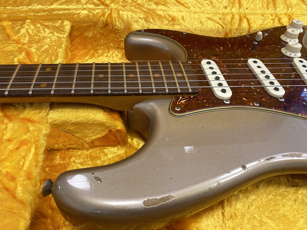 Vintage electric guitar with worn silver finish, rosewood fretboard, tortoiseshell pickguard, and three single-coil pickups on yellow velvet background