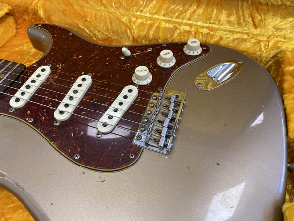 Close-up of vintage electric guitar body with tortoiseshell pickguard, three single-coil pickups, volume and tone knobs, and chrome bridge on a yellow plush background