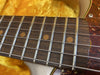 Close-up of a vintage electric guitar rosewood fingerboard with metal frets and dot inlays resting on a yellow plush guitar case interior