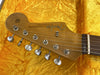 Close-up of Fender Stratocaster electric guitar headstock with vintage tuning pegs and original contour body logo on yellow plush guitar case interior
