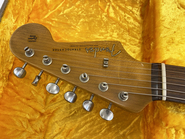 Close-up of Fender Stratocaster electric guitar headstock with vintage tuning pegs and original contour body logo on yellow plush guitar case interior