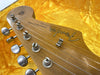 Close-up of vintage Fender Stratocaster guitar headstock showing tuning pegs and logo on wooden finish background with yellow fabric case lining