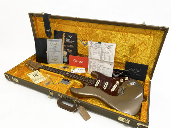 Fender custom shop electric guitar in gold finish with tortoiseshell pickguard, displayed in open vintage-style hardshell case with plush yellow interior, including Fender certificate of authenticity, owner's manual, setup documents, and guitar accessories.