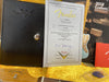 Fender Custom Shop Limited Edition Certificate of Authenticity for Ltd 60 Rstd Stratocaster Relic with Fender Custom Shop leather folder, 2018 Custom Guitar Design Guide, Fender guitar headstock, and guitar pick on yellow fabric background.