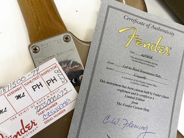 Close-up of Fender Limited Edition guitar neck plate with serial number CZ534789 alongside Fender Certificate of Authenticity for Ltd 60 Rstd Stratocaster Relic guitar with handwritten date and signature, and Fender inspection tag.