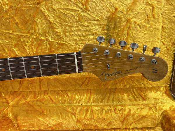 Close-up of Fender Stratocaster electric guitar headstock with tuning pegs and rosewood fretboard on yellow plush case lining
