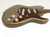 Vintage electric guitar with metallic gold finish, tortoiseshell pickguard, three single-coil pickups, and cream tone and volume knobs on white background, showing wear and scratches on body.