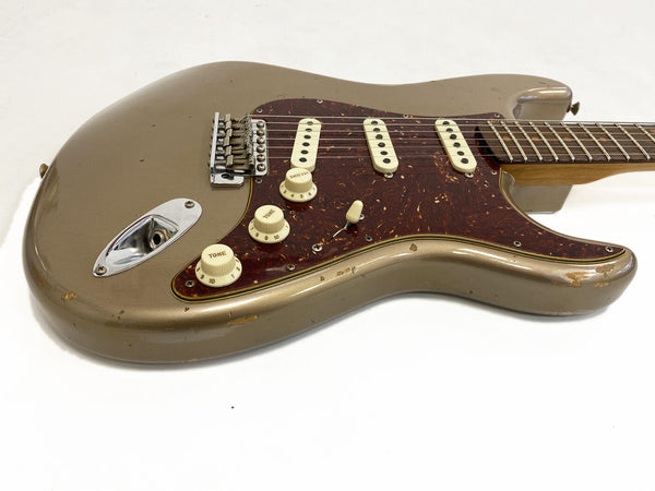 Vintage electric guitar with metallic gold finish, tortoiseshell pickguard, three single-coil pickups, and cream tone and volume knobs on white background, showing wear and scratches on body.