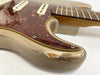 Close-up of a vintage electric guitar body showing worn gold finish and tortoiseshell pickguard with white single-coil pickups and chrome screws, featuring a maple neck with metal frets on a white background.